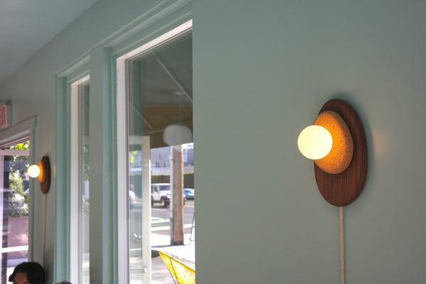 Pebble wall sconce turned on showing warm dimmable light above bed